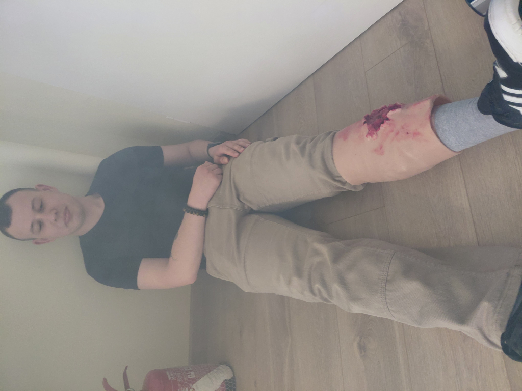 Szkolenie Bezpieczna Ewakuacja organizowane przez BON UWM, na zdjęciu leżący na podłodze  pozorant z imitacją otwartej rany lewej nogi.  