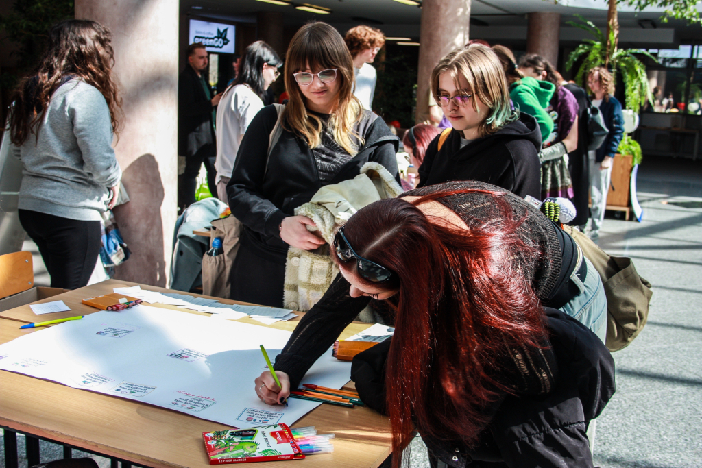 Warsztaty sensoryczne 2026  na zdjęciu trzy studentki pochylają się nad stołem z flamastrami kolorowymi i kartką papieru, jedna z nich coś pisze.