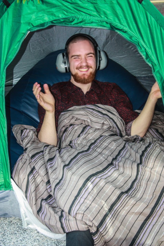 Student uśmiechający się ze słuchawkami nausznymi  leżący na niebieskiej pufie pod kocem